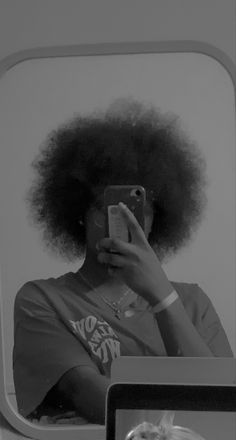 a woman taking a selfie in front of a mirror with an afro hair style