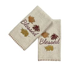 two white towels with embroidered leaves on them and the words blessed written in red ink