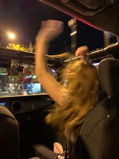 a woman sitting in the back seat of a car with her arms up and hands raised