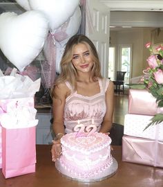 a woman sitting in front of a cake with candles on it and presents behind her