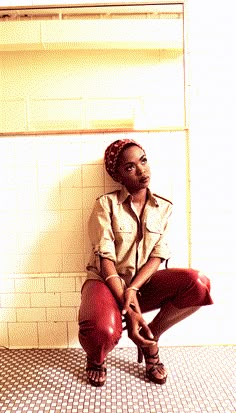 a woman sitting on top of a red chair in a bathroom next to a tiled wall