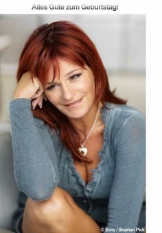 a woman with red hair is smiling and posing for the camera, she has her hand on her head