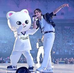 two people dressed in white performing on stage with one person holding a microphone and the other standing up