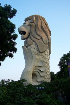 a statue of a lion with its mouth open in front of some trees and bushes