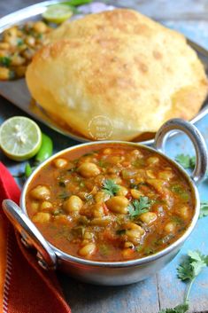 a bowl of chickpea stew with bread and limes in the background on a blue surface