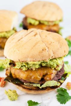 two burgers with guacamole and lettuce on them sitting on a marble surface