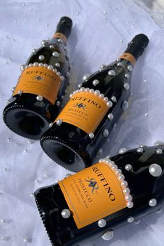 three bottles of wine sitting on top of a white cloth covered table with silver beads