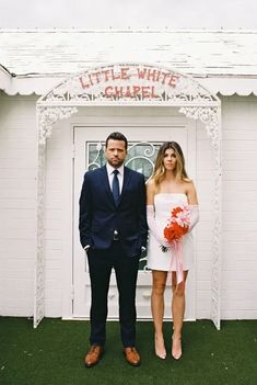 a man and woman standing next to each other in front of a small white building