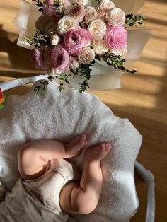 a baby laying on top of a white blanket next to a bouquet of pink and white flowers