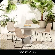 a white table with four chairs around it on a wooden floor next to potted plants