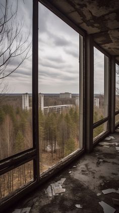 an abandoned building with broken windows looking out at the trees and buildings in the distance