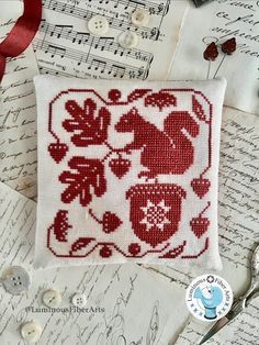 a red and white cross stitched square on top of sheet music with scissors next to it