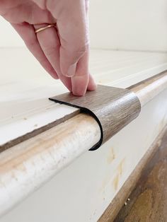 a hand is touching the edge of a window sill with a piece of wood