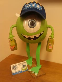 a green monster wearing a hat and holding two bags on top of a wooden table