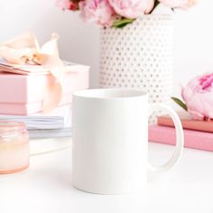 a white coffee mug sitting on top of a table next to pink and white flowers