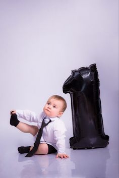 a baby wearing a tie sitting next to an inflatable giraffe