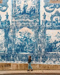 a woman standing in front of a blue and white wall with many paintings on it