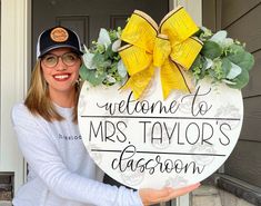 a woman holding a welcome to mrs taylor's classroom sign