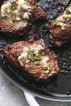 three steaks cooking in a skillet with herbs on top and cheese on the side