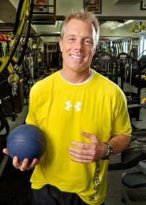 a man in a yellow shirt holding a blue ball and standing next to a gym