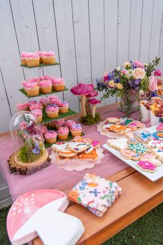 a table topped with lots of cupcakes and cakes next to a vase filled with flowers