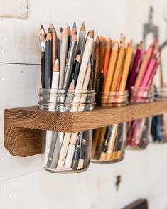 several pencils are lined up in mason jars on a shelf with wood brackets and hooks