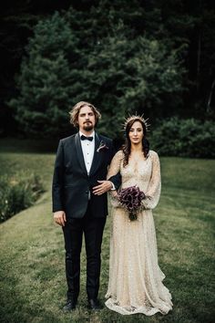 a man and woman in formal wear standing next to each other on grass with trees in the background