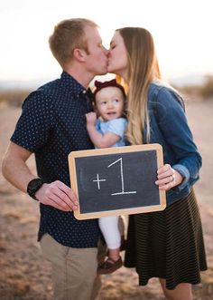 a man and woman kissing while holding a baby in front of a chalkboard with the number one written on it