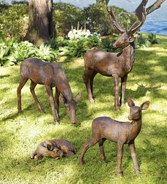 four bronze deer statues in the grass near trees and water with blue sky behind them