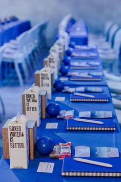 a long table is set up with blue and white tables cloths, pens, and boxes