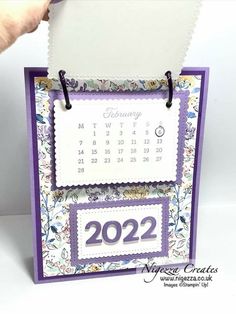 a hand holding up a calendar with the date on it and purple trimmings