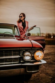 a woman leaning on the hood of an old red car with her hand out in front