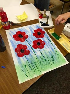 someone is painting red flowers on a piece of paper with watercolors and glue