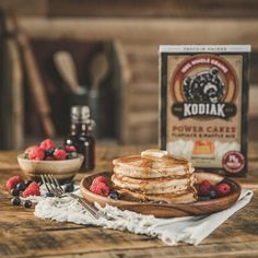 some pancakes and strawberries on a wooden table with kodiak coffee in the background