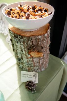 a bowl filled with nuts sitting on top of a wooden table next to a tree