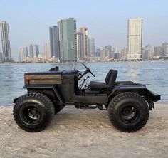 an old jeep is parked on the beach in front of some tall buildings and water