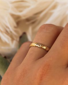 a woman's hand with a gold ring on her finger and a white flower in the background