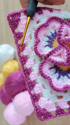 a crocheted granny's square being worked on by someone using a knitting needle