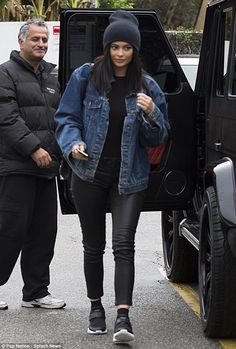 a woman in black pants and a denim jacket is stepping out of a vehicle