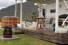 a hot tub sitting on top of a wooden deck next to a white house with mountains in the background