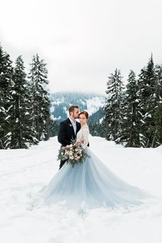 a bride and groom standing in the snow with pine trees behind them on their wedding day