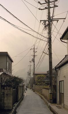 an empty street with power lines above it and houses on the other side in the distance