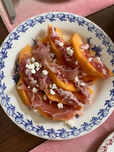 a white and blue plate topped with peaches covered in cheese on top of a pink table cloth