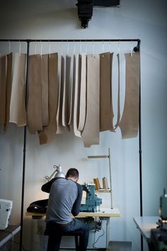 a man sitting at a sewing machine in front of some clothes hanging on a rack