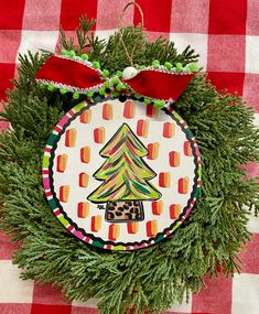 a christmas ornament hanging on a red and white checkered tablecloth with a tree