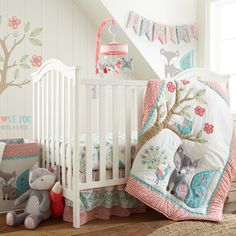 a baby crib bedding set with animals and trees on the wall next to it