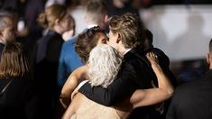 two people hugging each other in front of an audience at a formal event with one person wearing a black suit and the other white