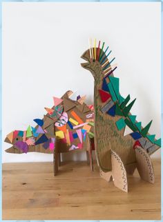 two cardboard dinosaurs made to look like they are standing next to each other on a wooden table