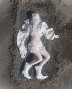 an aerial view of a woman in white clothing and boots laying on the ground with her arms outstretched