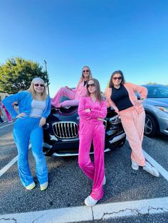 three women in pink and blue outfits standing next to a bmw car on the street